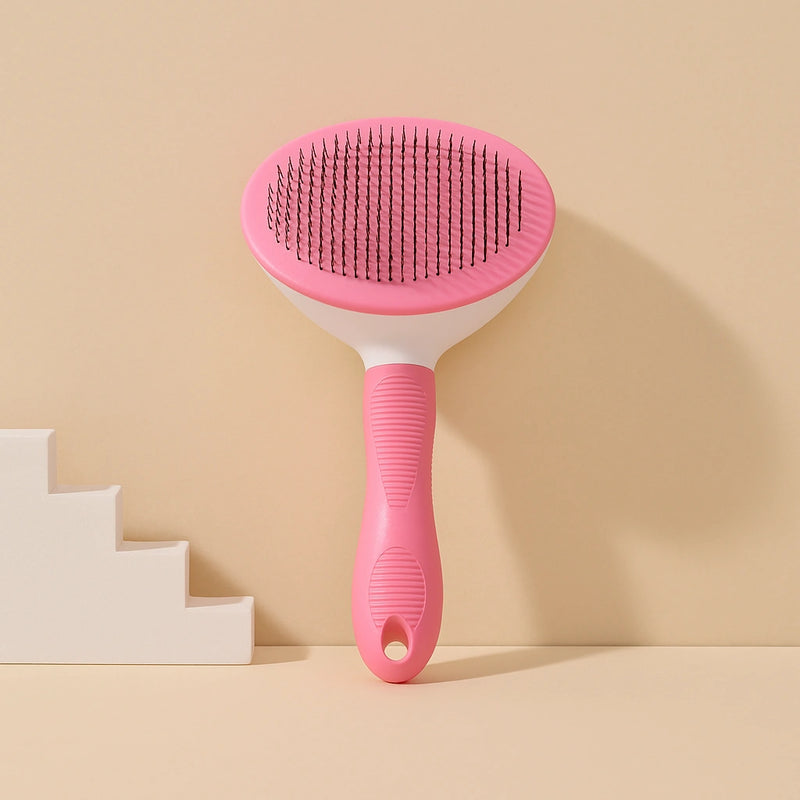 Spazzola autopulente per animali con manico rosa antiscivolo e setole in acciaio, fotografata in stile professionale su sfondo azzurro e beige.