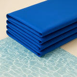 Tappetini refrigeranti blu piegati su fondo chiaro con riflessi d’acqua, ideali per l’estate e facili da riporre
